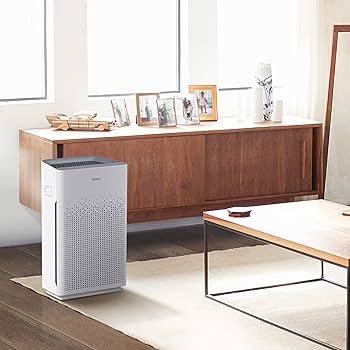 White Winix AM90 Wi-Fi Air Purifier on rug in bright, modern living room with wooden furniture and window light.