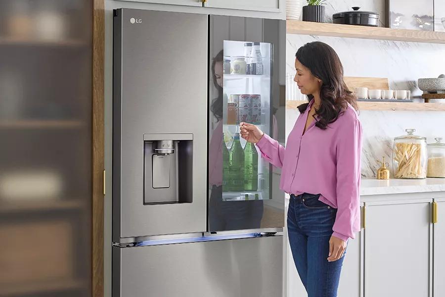 Woman accessing beverages from LG InstaView Door-in-Door refrigerator in a modern kitchen.