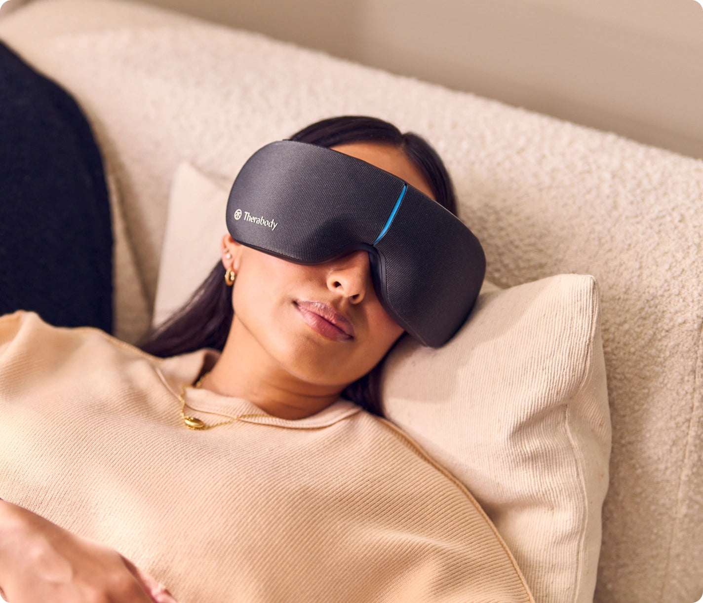 Woman comfortably resting on a couch, wearing Therabody SmartGoggles for relaxation.