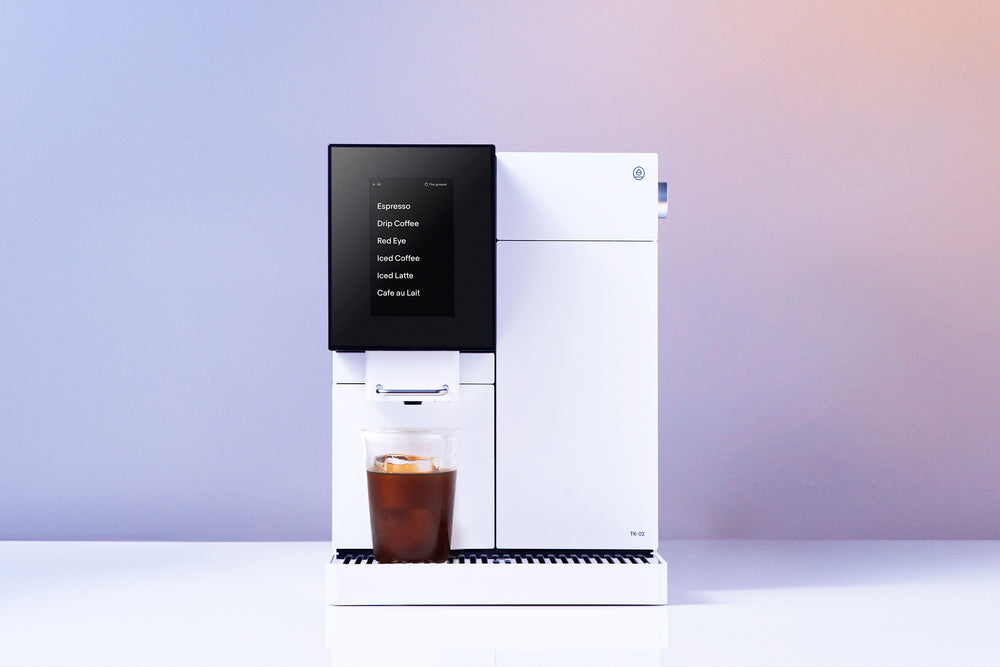 White Terra Kaffe TK-02 automatic coffee machine displaying a menu of drinks and a glass of iced coffee on the drip tray.