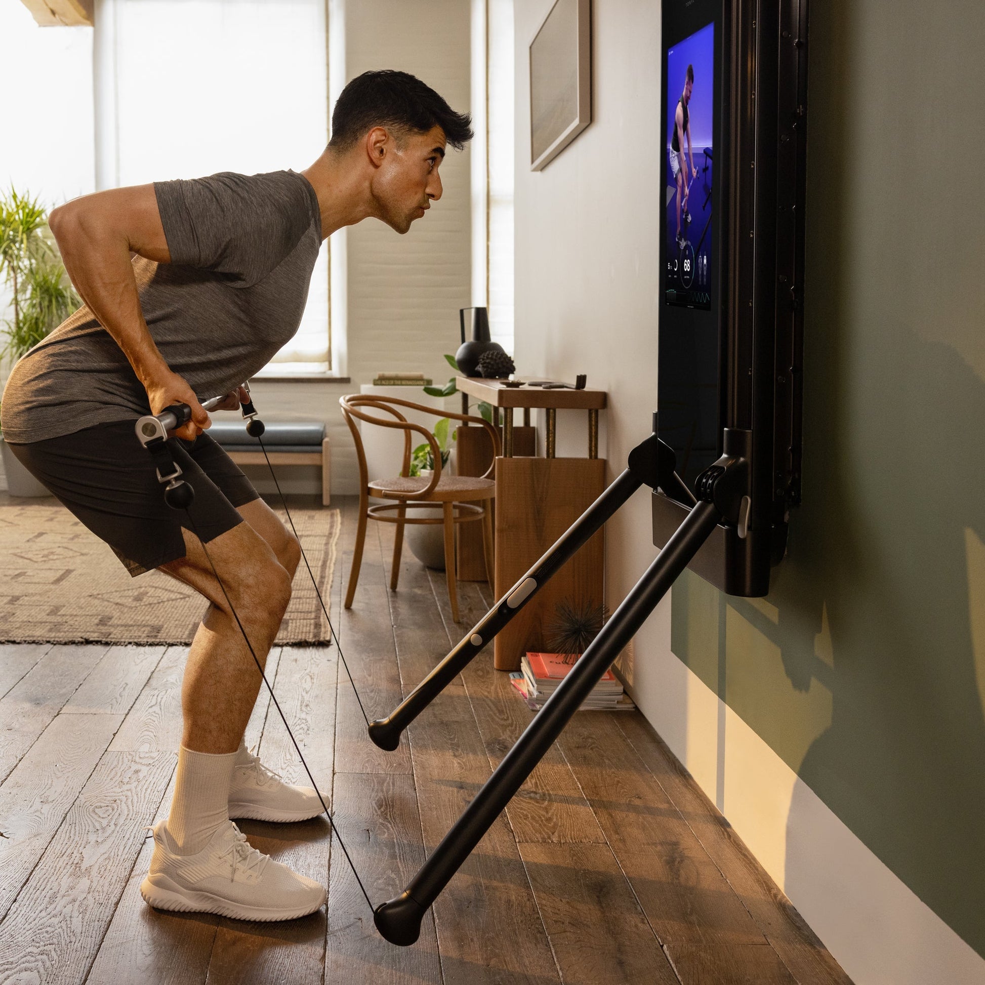 Man in activewear performing a cable row exercise on a Tonal smart home gym in a well-lit living room.