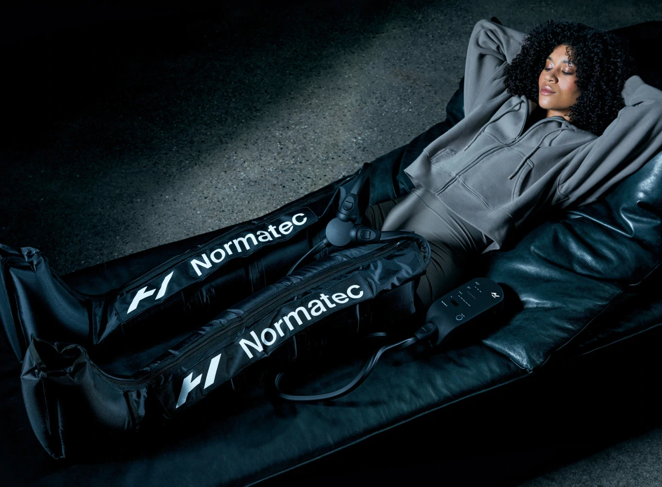 Woman relaxing on a couch, using Hyperice Normatec 3 Legs compression boots for muscle recovery and wellness.