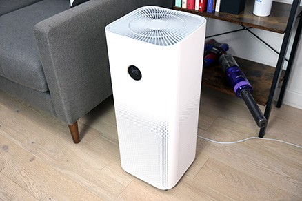 White Xiaomi Smart Air Purifier 4 Pro on wood floor next to a gray couch in a living room.