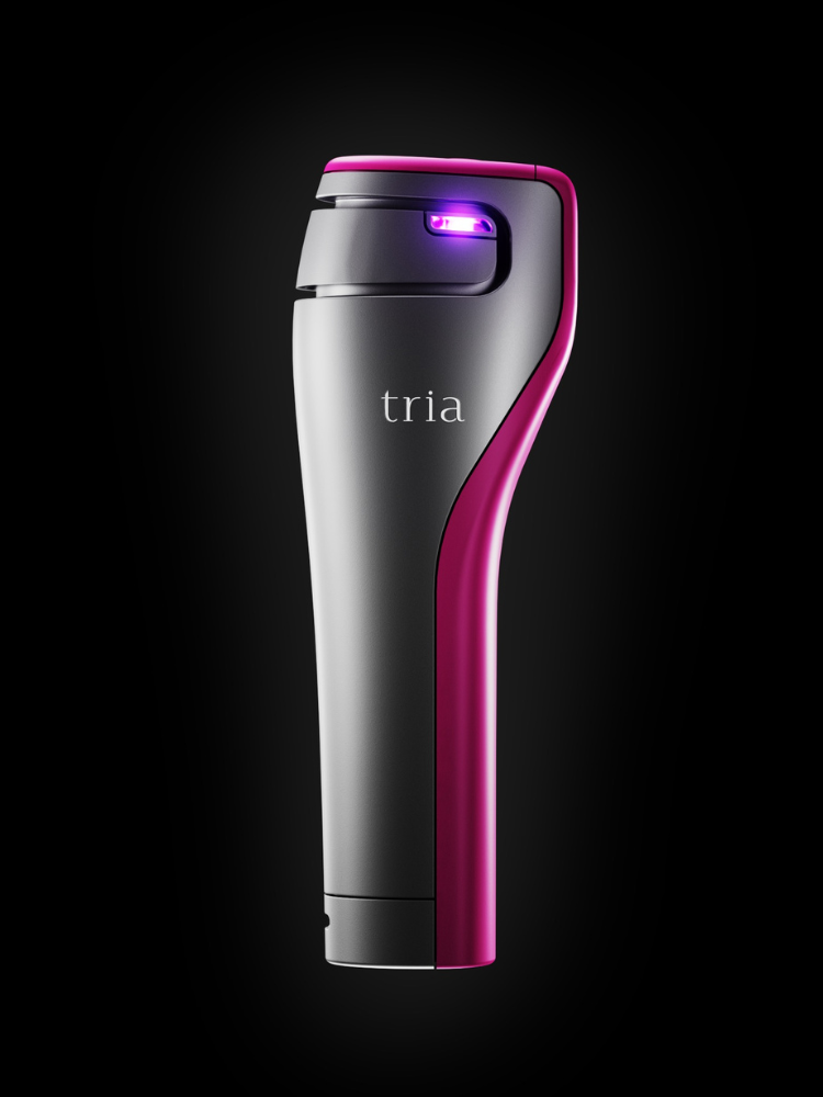 Sleek pink and grey Tria Age-Defying Laser handheld device with glowing purple light, for at-home anti-aging skin treatment.